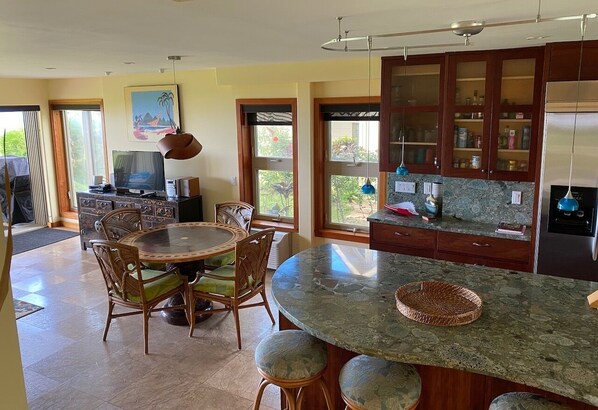 A spacious kitchen with a dining area, large windows, and a stone countertop. - Puamana Ocean Front Tropical Paradise 226-1 (Lahaina)