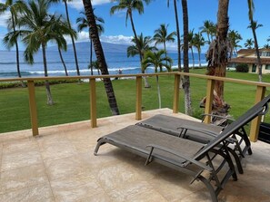 A balcony with two lounge chairs, a view of the ocean, palm trees, and a grassy area. - Puamana Ocean Front Tropical Paradise 226-1 (Lahaina)