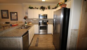 Kitchen features a refrigerator, oven, microwave, granite countertop, and wooden floor.