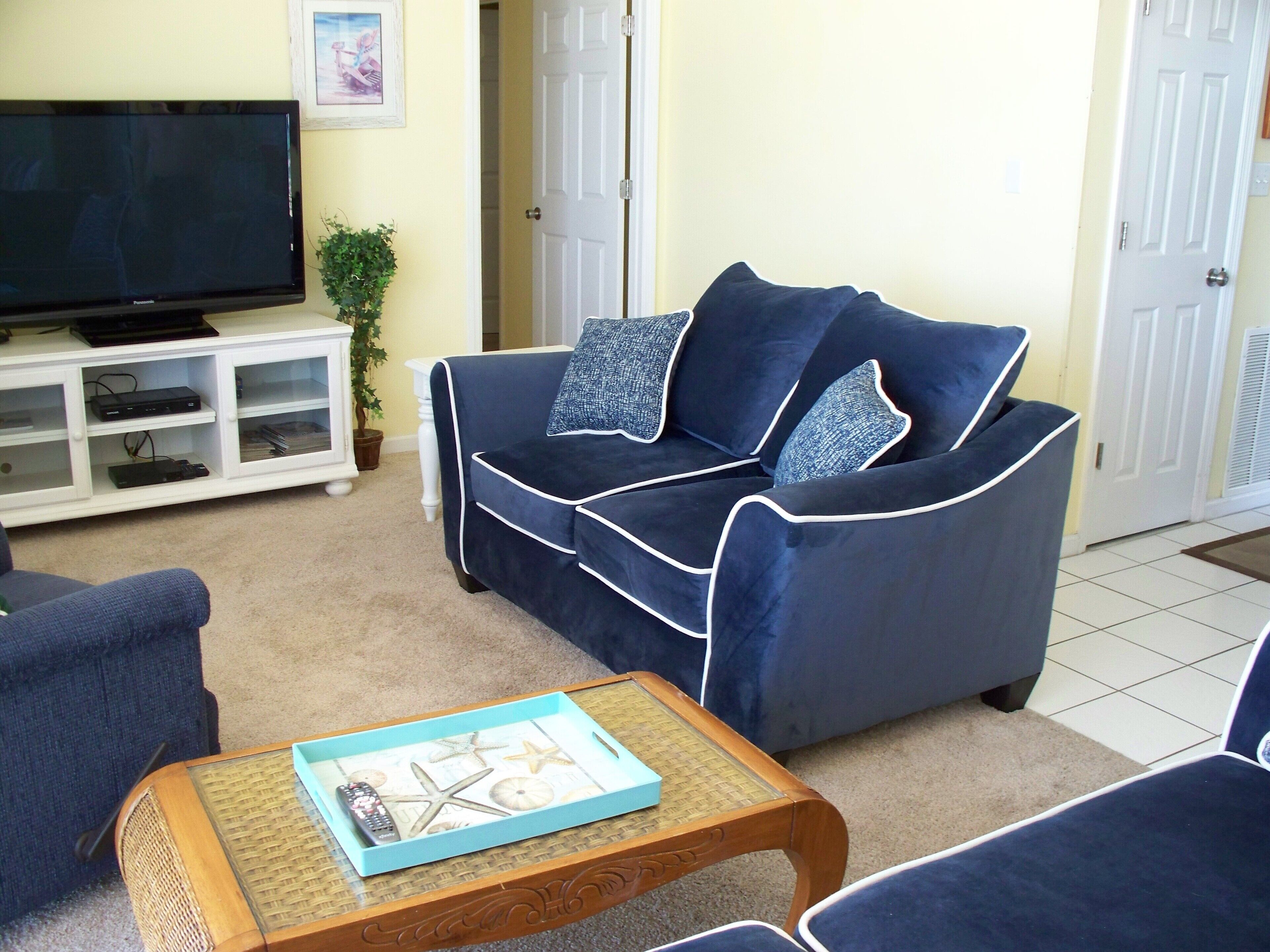 Un salón con un sofá azul oscuro, un televisor sobre un mueble bajo y una mesita con una bandeja.
