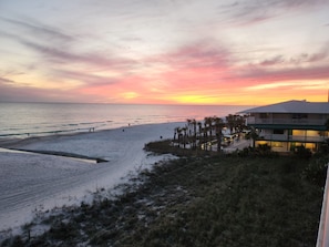A beach with a building that has multiple floors and balconies, overlooking the ocean.