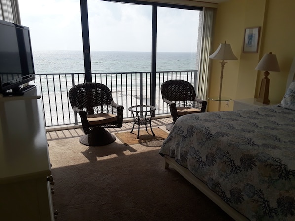 A balcony with a bed, two wicker chairs, a small table, and a TV.