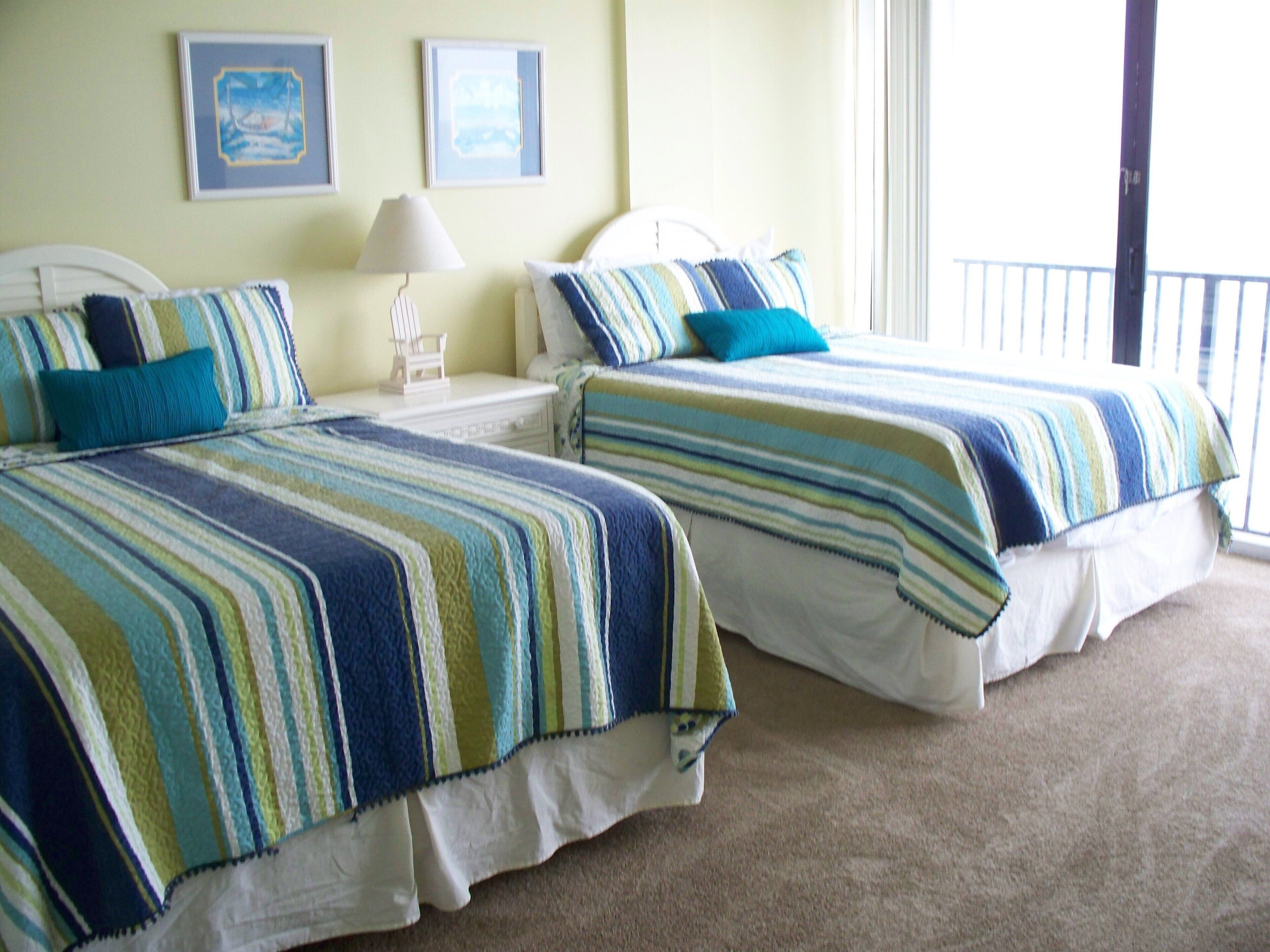Two twin beds with striped bedding, a nightstand with a lamp, and framed pictures on the wall.