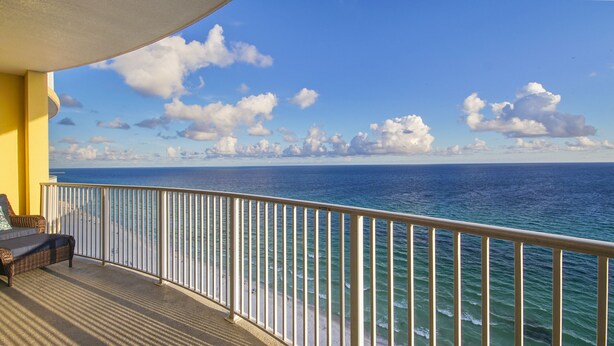 Un balcon donnant sur l’océan, avec une balustrade blanche et un fauteuil en osier.