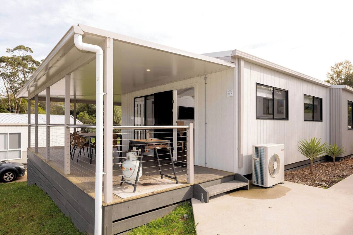 Een moderne stacaravan met een overdekte veranda, een gasfles en een airconditioner.