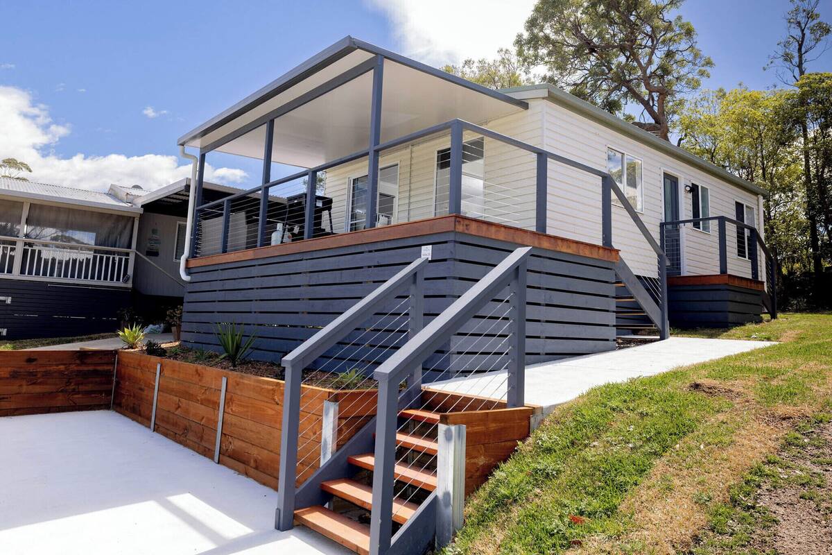 Een modern huis met twee verdiepingen, een overdekte veranda, een houten terras en een trap naar de bovenverdieping.