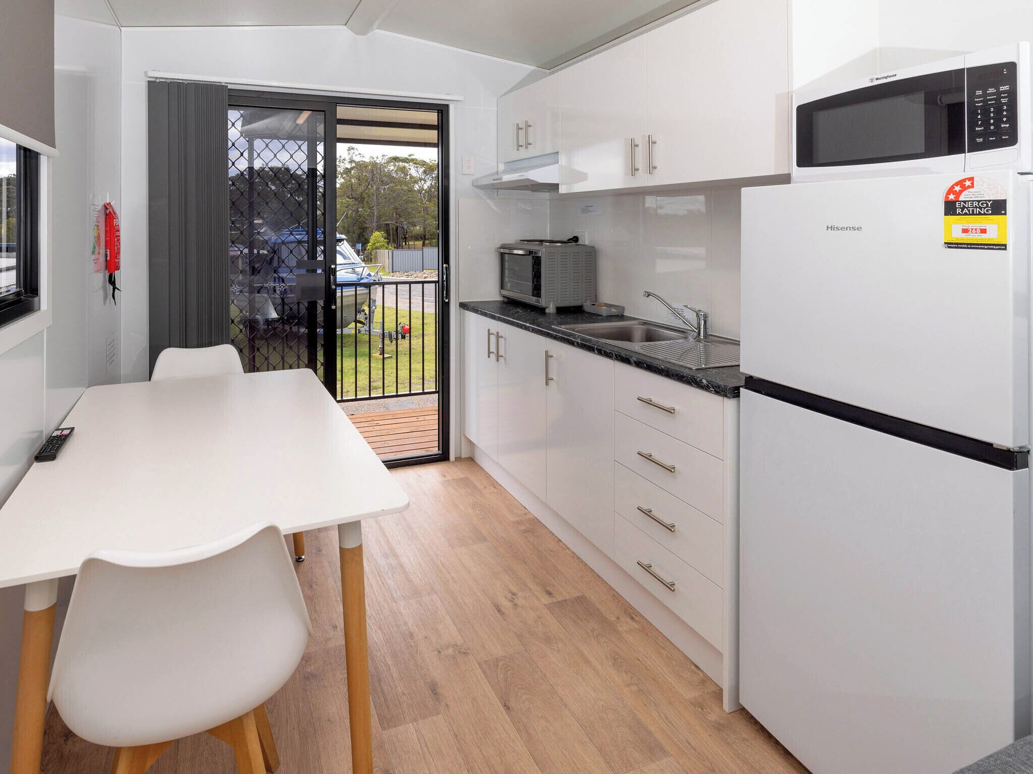A compact kitchen with white cabinets, a microwave, a sink, and a Hisense refrigerator.
