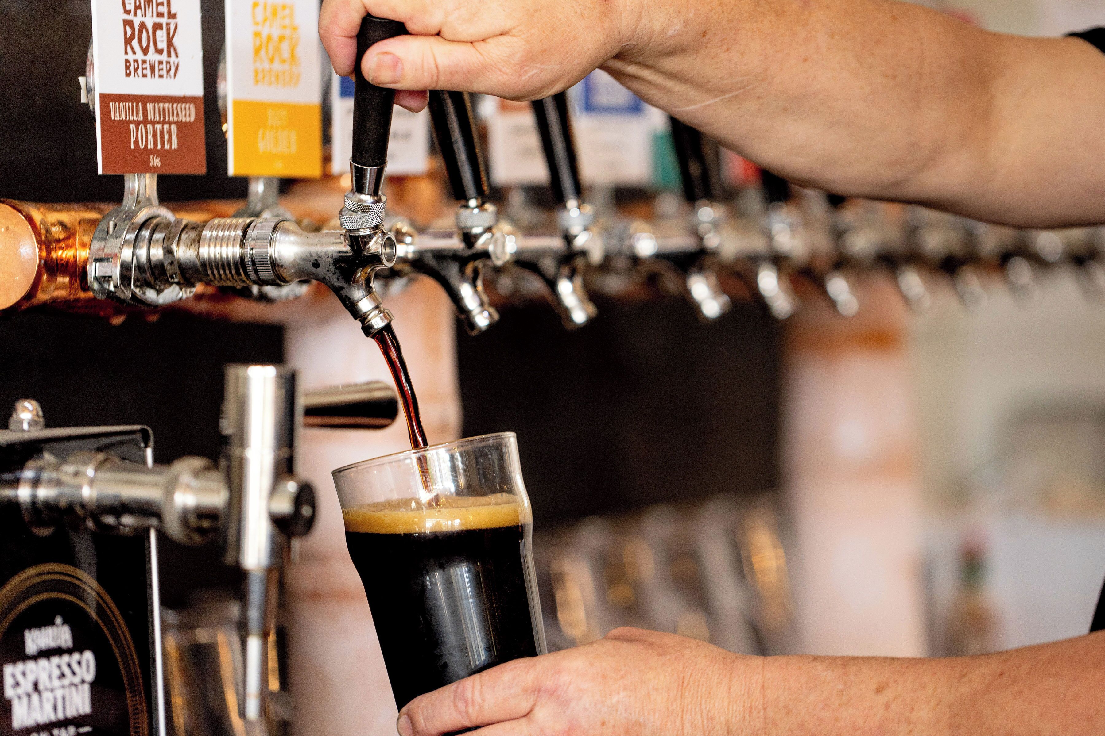 A hand pouring a dark beverage from a tap labeled "Camel Rock Brewery Vanilla Wattlesd Porter."