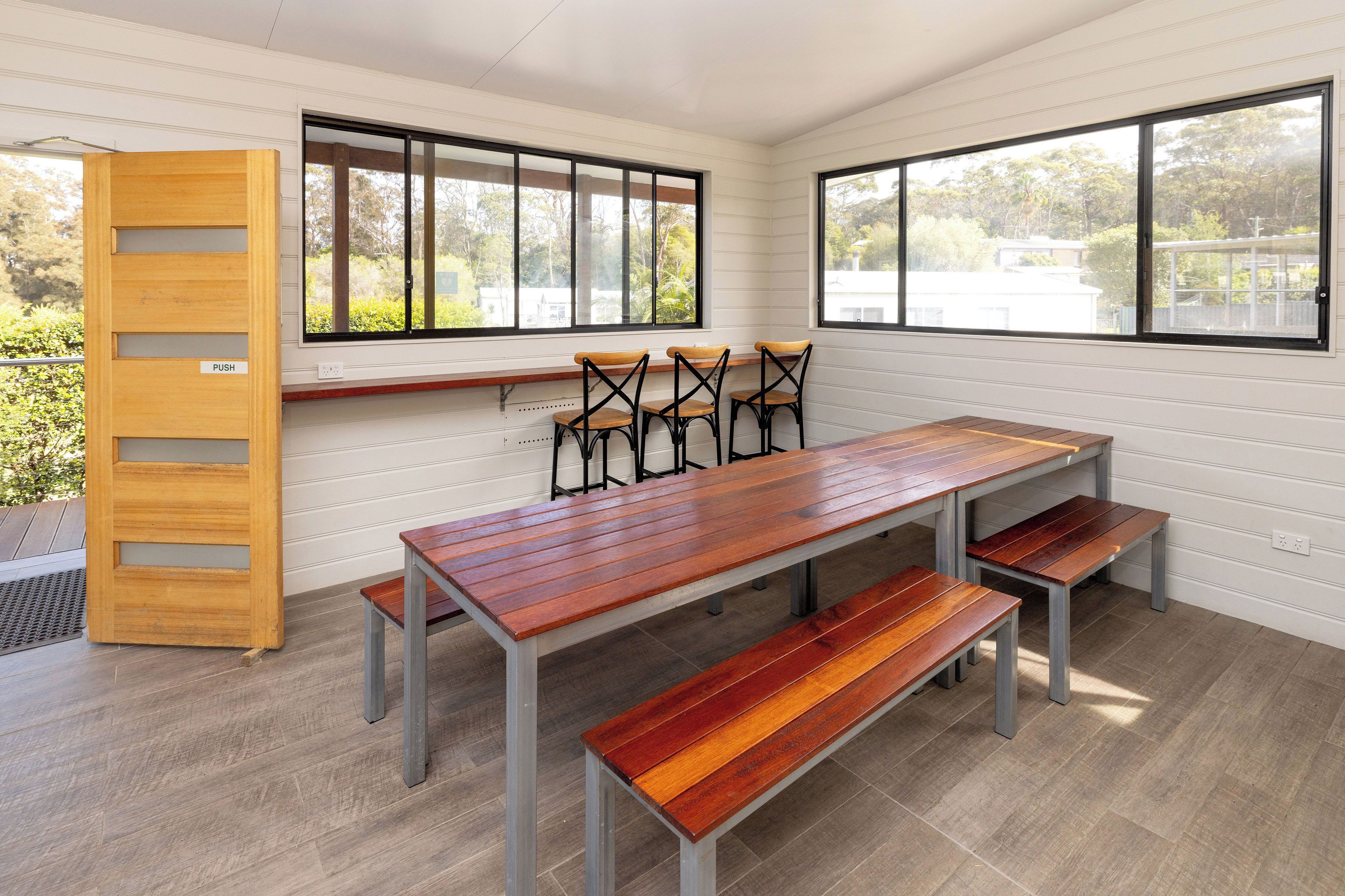 A dining area with a wooden table and benches, large windows with black frames, and a wooden push-up board.