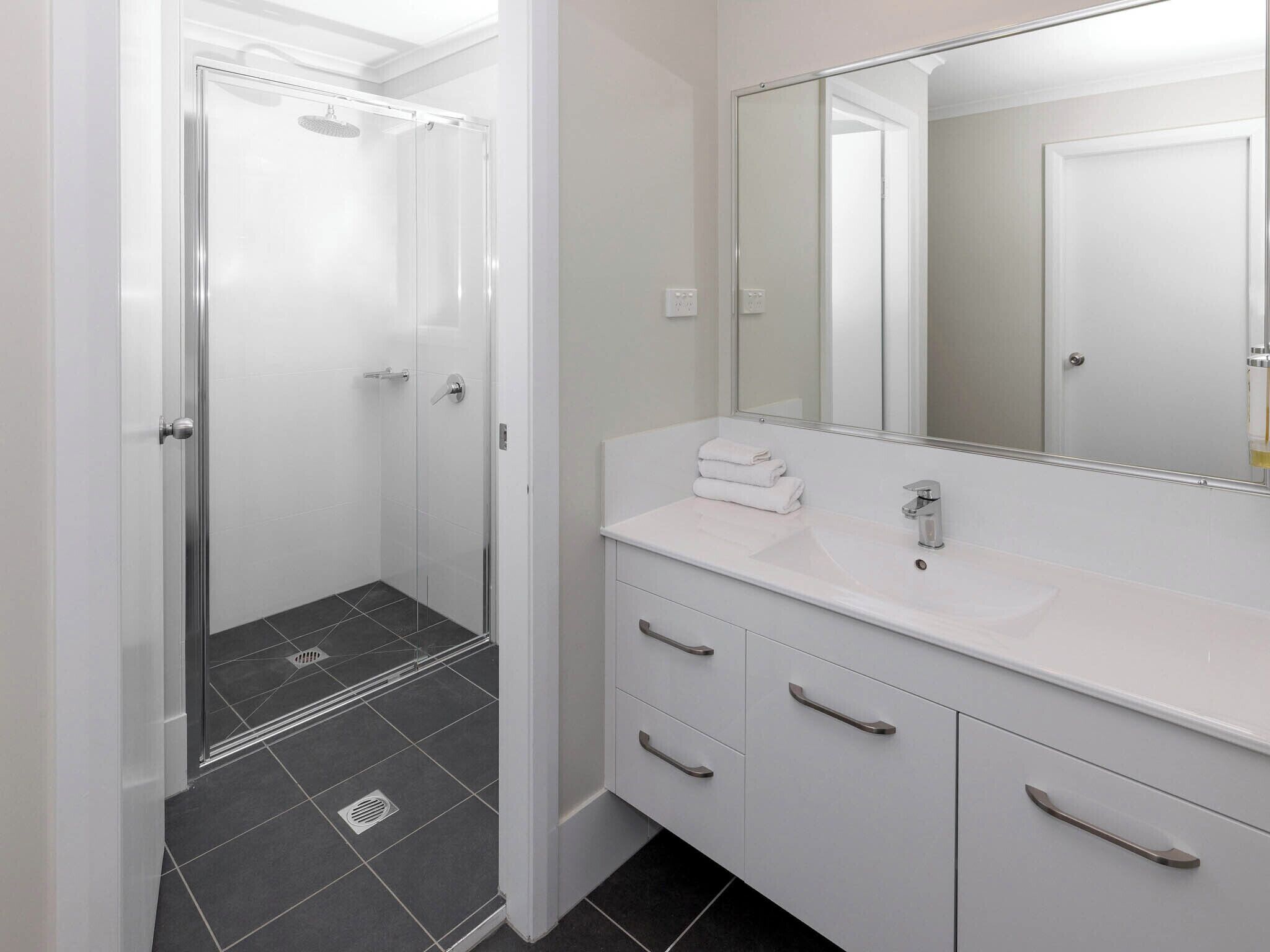 A modern bathroom with a glass-enclosed shower, a white vanity with a large mirror, and a tiled floor.