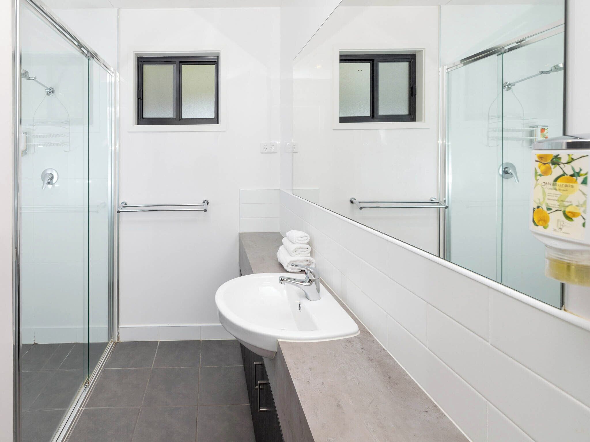 A modern bathroom with a glass shower enclosure, a white sink, and a small window above the mirror.