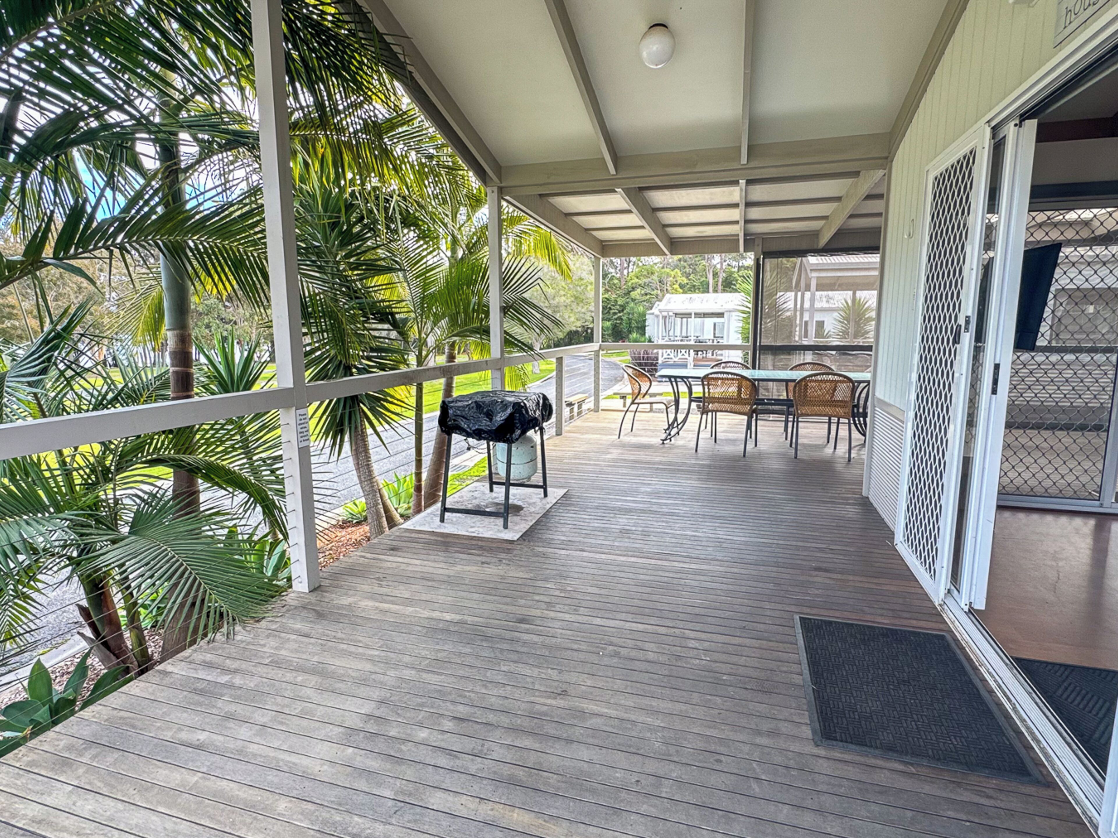 A covered outdoor area with a wooden deck, a grill, and a table with chairs.