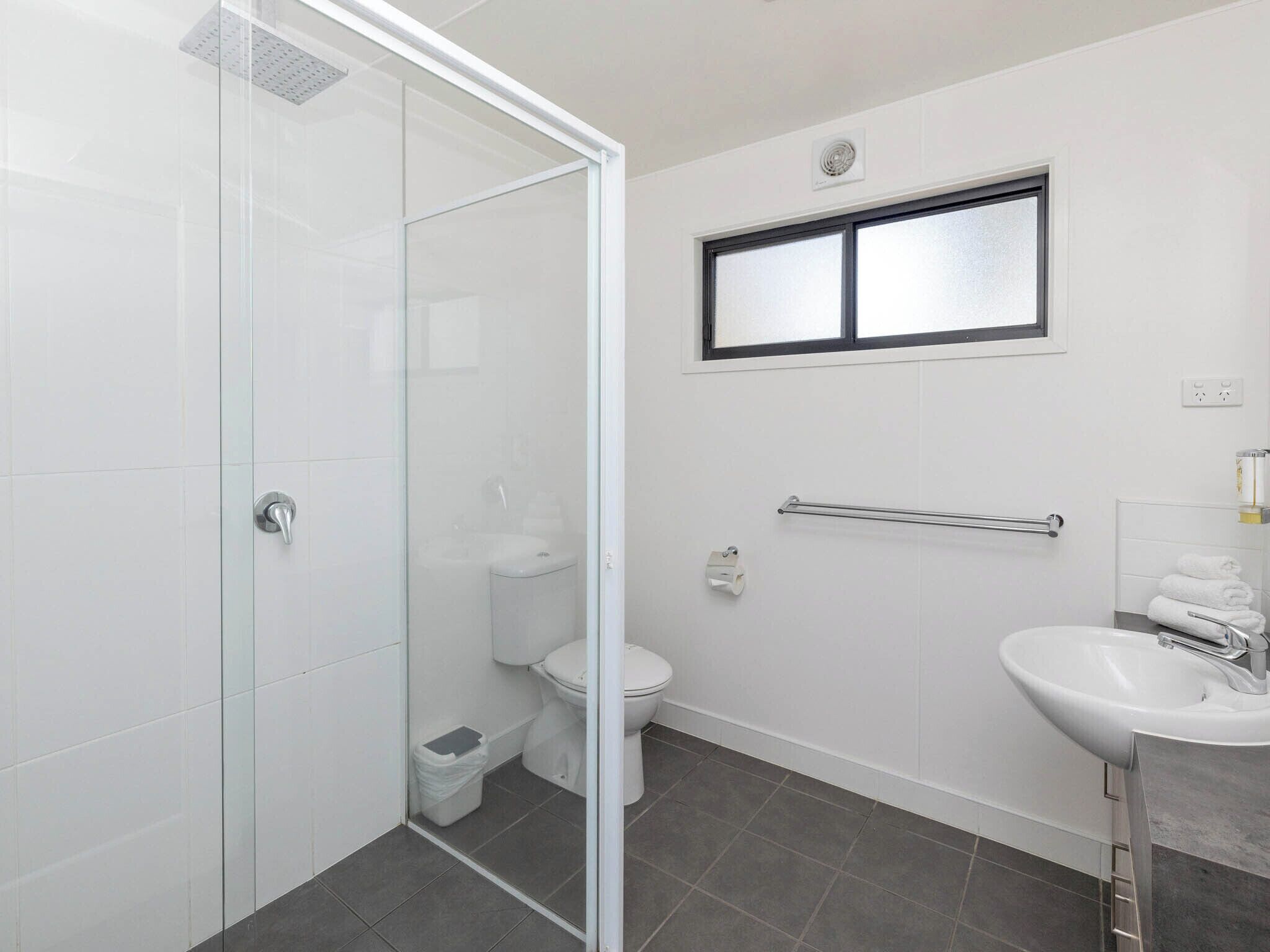 Un baño moderno con cabina de ducha de vidrio, inodoro, lavamanos y toallero.