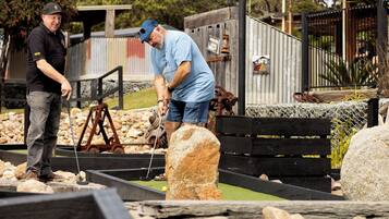 Un parcours de mini-golf avec un banc en bois, une porte en métal et un panneau indicateur en arrière-plan.