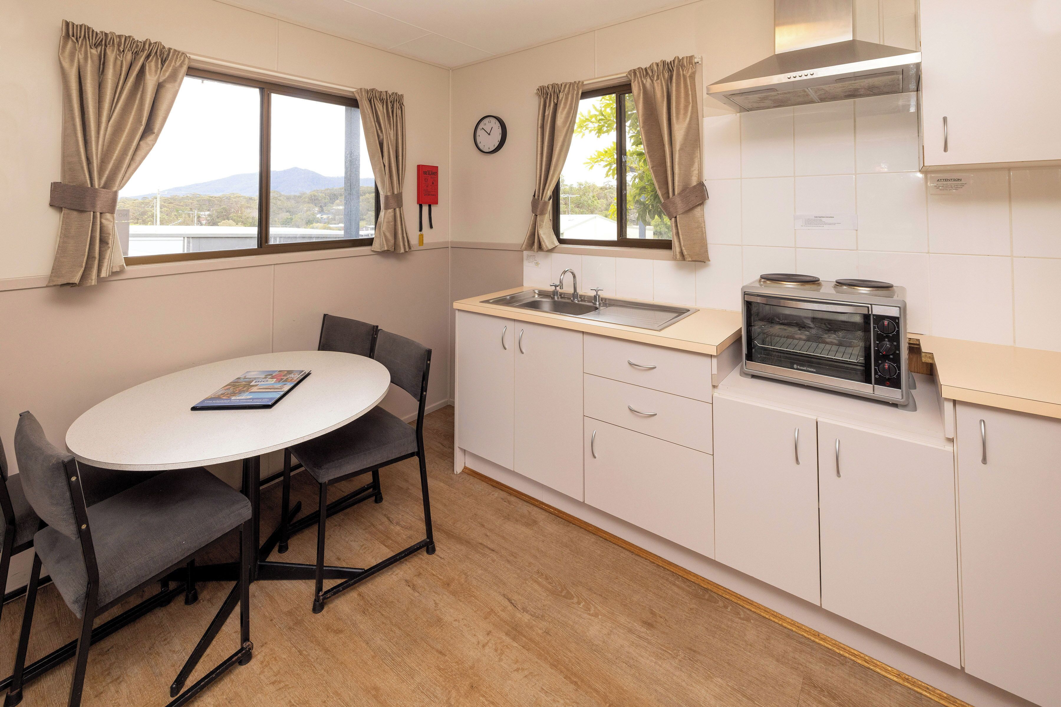 A compact kitchen with a round table, two chairs, a sink, a stove, and cabinets.