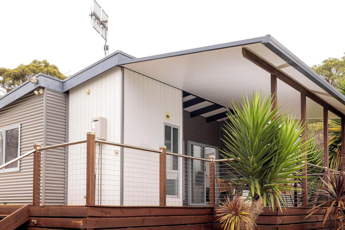 Een tweelaags huis met een overdekte veranda, een schotelantenne en een houten terras.