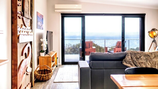 Una sala de estar moderna con un amplio ventanal corredera que da a un balcón con vistas al mar.
