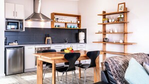 Una cocina moderna con microondas, estufa y lavavajillas. Hay una mesa de comedor de madera con sillas y una cafetera.