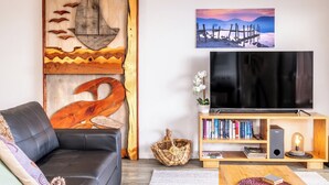 Una sala de estar con un sofá de cuero negro, una estantería de madera, un televisor de pantalla plana y una pared decorada con una obra de arte de madera y un cuadro enmarcado.