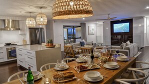 A modern kitchen with a dining area, featuring a large island, stainless steel appliances, and a flat-screen TV. - Hidden Oasis - Peregian Beach (Peregian Beach)