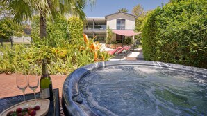 A hot tub surrounded by lush greenery, a poolside area with lounge chairs, and a building in the background. - Hidden Oasis - Peregian Beach (Peregian Beach)