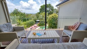A balcony with wicker furniture, a table, and a view of a pool and greenery. - Hidden Oasis - Peregian Beach (Peregian Beach)