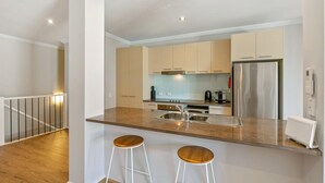 A modern kitchen with a central island, stainless steel appliances, and two bar stools. - Beachy Keen - sleeps 11 (COWES)