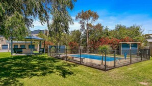 A backyard with a swimming pool, a covered patio, and a fenced area with trees and shrubs. - Beachy Keen - sleeps 11 (COWES)