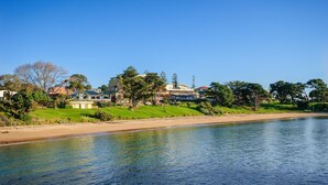A riverside view with a sandy beach, grassy areas, and buildings in the background. - Beachy Keen - sleeps 11 (COWES)