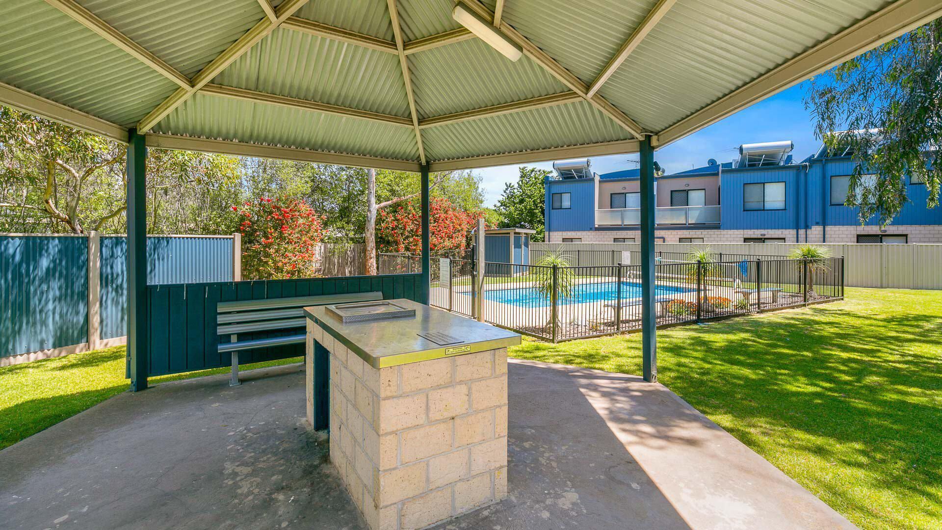 Un espacio exterior techado con piscina, bancos y una estación de barbacoa.