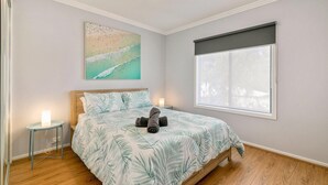 A bedroom with a bed, a nightstand, a wall art, and a window. - Beachy Keen - sleeps 11 (COWES)