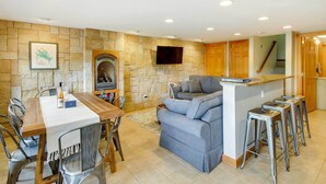 A spacious living area with a stone wall, a fireplace, a grey sofa, a wooden dining table, and a TV mounted above the fireplace. - Laconia Home w/ Beach - 1/2 Mi to Weirs Beach (Laconia)