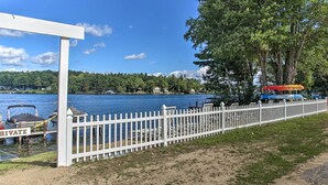 A lakeside view with a white fence, docked boats, and a covered area. - Laconia Home w/ Beach - 1/2 Mi to Weirs Beach (Laconia)