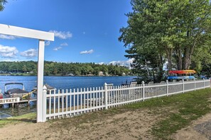 A lakeside view with a white fence, docked boats, and a covered area. - Laconia Home w/ Beach - 1/2 Mi to Weirs Beach (Laconia)