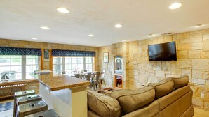 A modern kitchen with a stone backsplash, a built-in TV, and a bar area with stools. - Laconia Home w/ Beach - 1/2 Mi to Weirs Beach (Laconia)