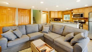 A modern kitchen with wooden cabinets, a grey sectional sofa, and a coffee table with remote controls. - Laconia Home w/ Beach - 1/2 Mi to Weirs Beach (Laconia)