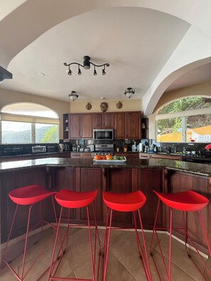 A kitchen with a large island, wooden cabinets, and red bar stools.