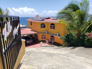Un edificio amarillo con paneles solares, techo rojo y vista al océano.