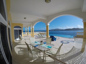 Un espacio al aire libre cubierto con mesa y sillas, piscina y vista al mar.