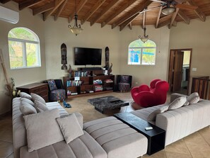 A spacious living room with a large sectional sofa, a red accent chair, a flat-screen TV, and a bookshelf filled with books and decorative items.