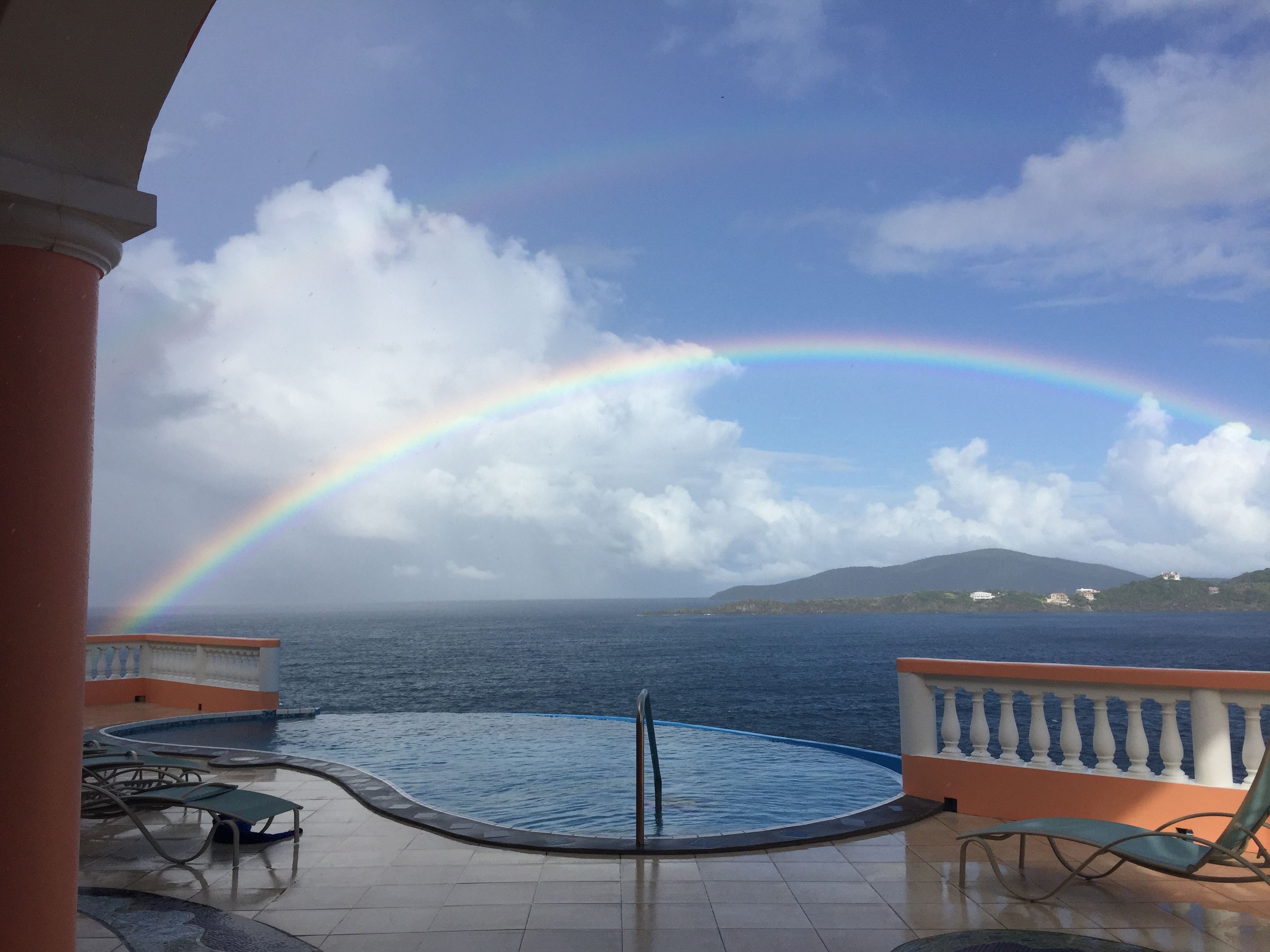 Un espace piscine offrant une vue sur la mer et un arc-en-ciel.