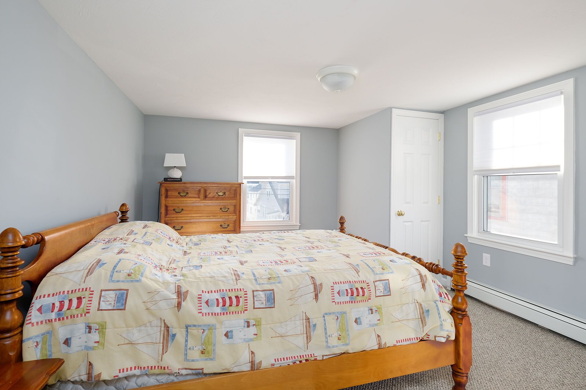 A bedroom with a wooden bed, a dresser, and two windows.