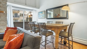Ein Essbereich mit Holztisch und Stühlen, einer Couch mit orangefarbenen Kissen, einem großen Spiegel und einer Karte an der Wand.