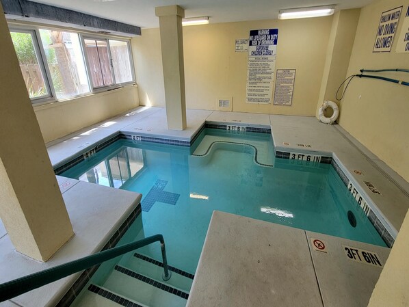 An indoor swimming pool with safety signs, a lifebuoy, and a pool capacity sign. - Spacious Retreat 1/2 Block From The Beach! + Pool Access. (Tybee Island)