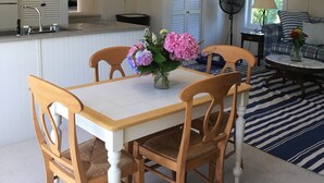Un comedor con una mesa y sillas, un jarrón con flores y un ventilador.