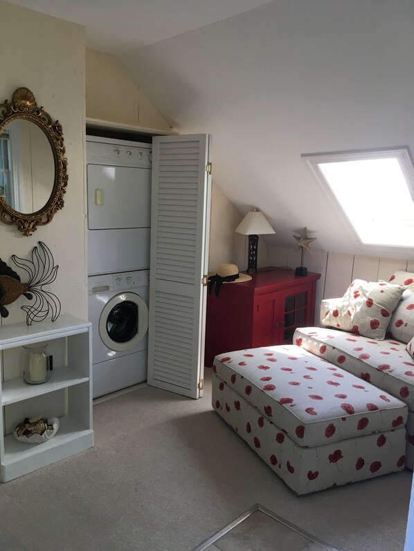 A compact bedroom with a washing machine, a red cabinet, a white sofa with a floral pattern, a star decoration, and a skylight.