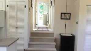 Un pasillo con una escalera alfombrada, puertas blancas y un cubo de basura.