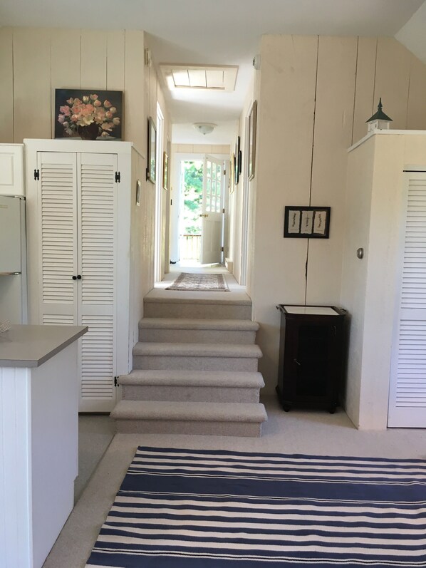 A hallway with a carpeted staircase, white doors, and a trash bin.