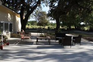 An outdoor patio with a table and chairs, surrounded by large trees and a building. - Beautiful hill country peace. (Blanco)