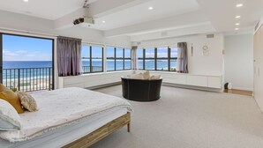 A spacious bedroom with a large bed, a black ottoman, and a view of the ocean.